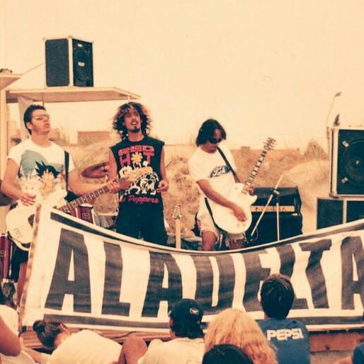 Aladelta tocando frente a una bandera con el nombre de la banda